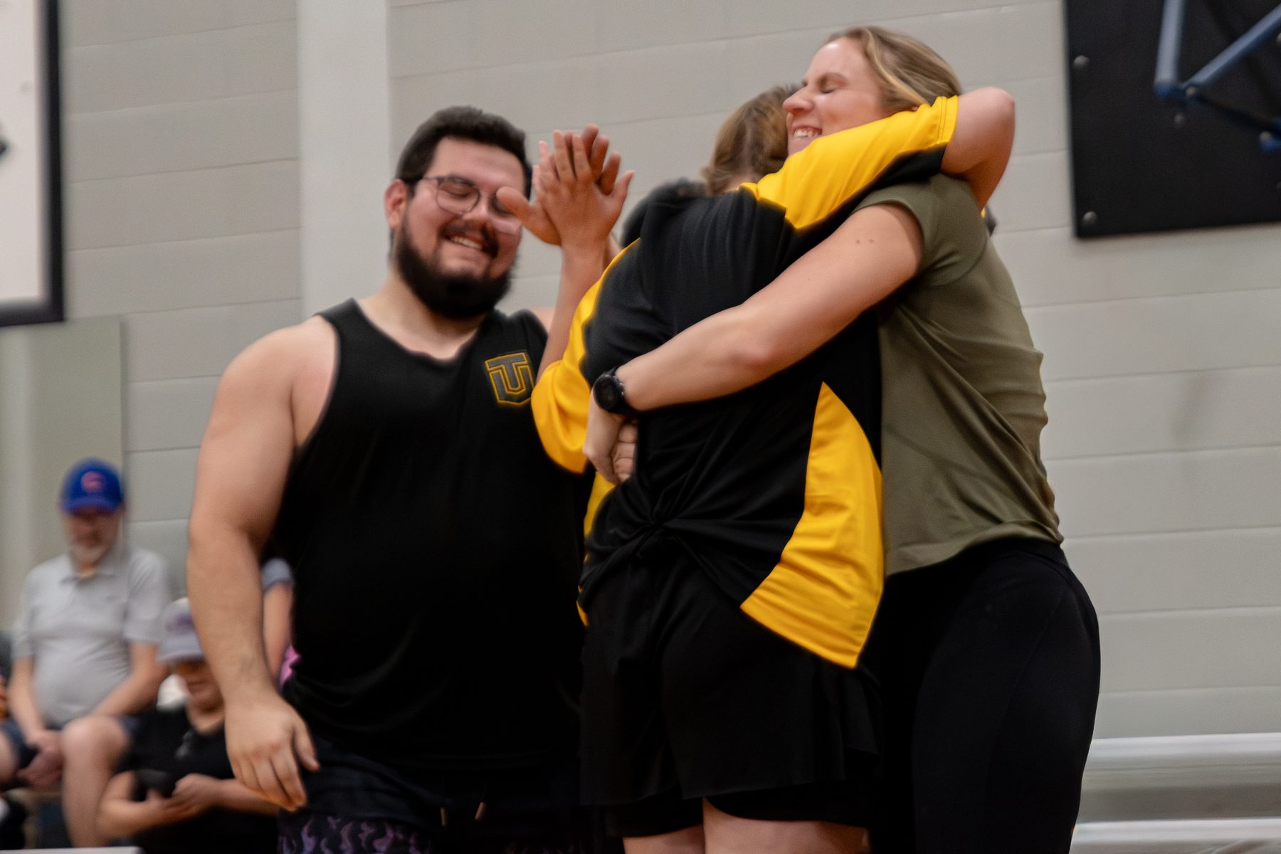 An athlete and a woman in a Train Unique shirt hug while a man beside them smiles
