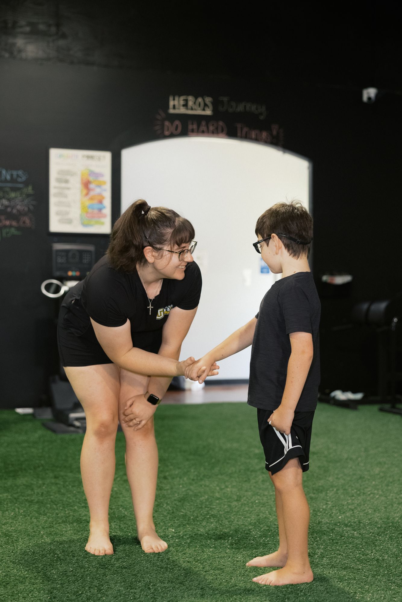 A coach leans down to shake hands with a young athlete at eye level