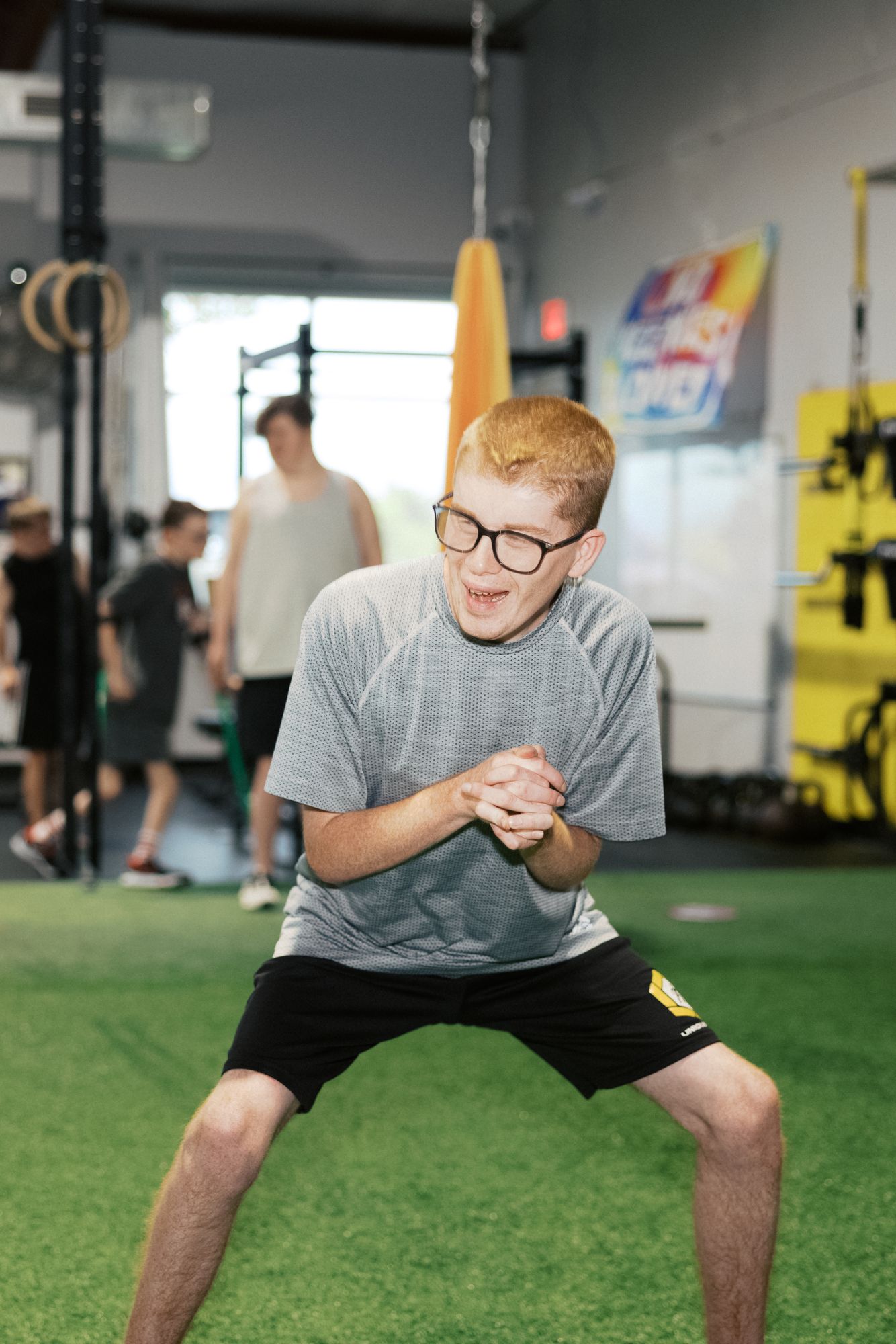 An athlete in glasses holds a squat on the turf, hands clasped, smiling