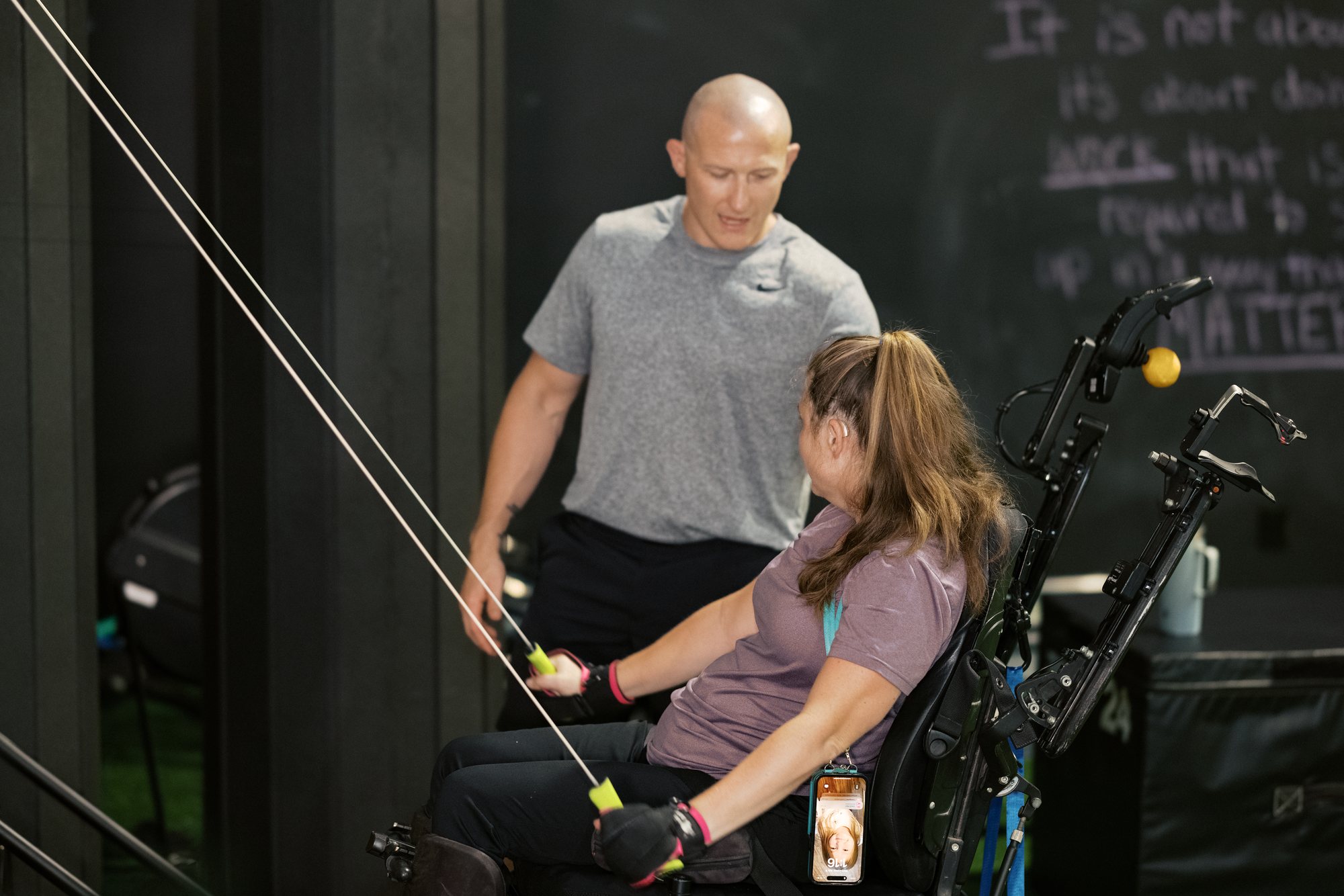 Damon watches closely as an athlete, seated in her chair, pulls two cable handles toward her